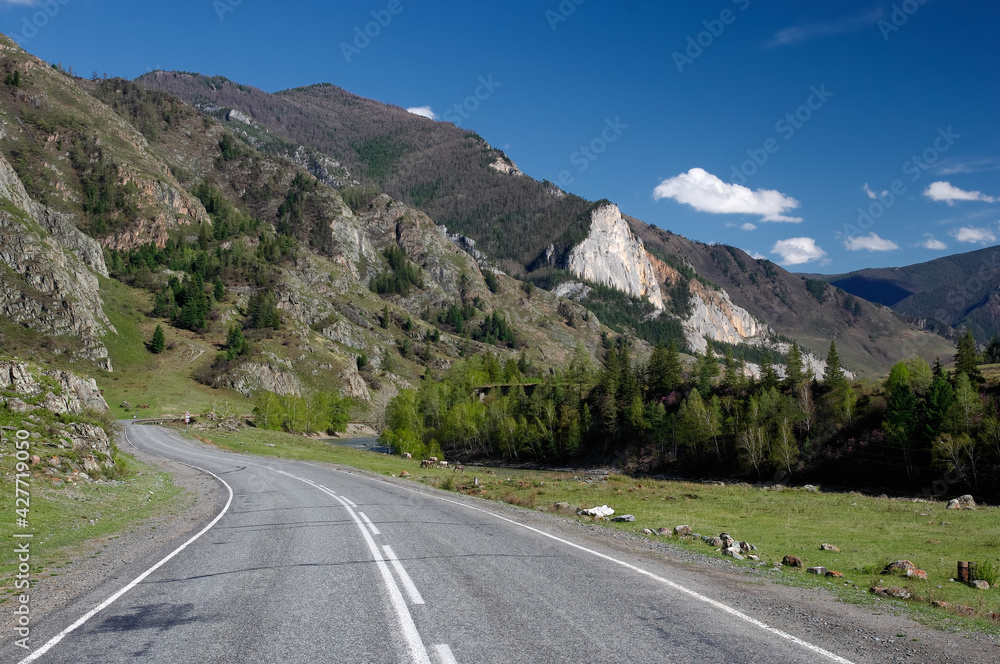 Road asphalt path through a rocky pass at the background of the high ranges under a blue sky