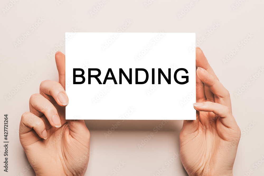 Female hands hold card paper with text branding on a yellow background. Business and finance concept Female hands hold card paper with text branding on a yellow background. Business and finance concept