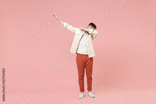 Full length young trendy fashionable fun friendly caucasian man in jacket white t-shirt do dab hip hop dance hands move gesture youth sign hiding cover face isolated on pastel pink background studio.