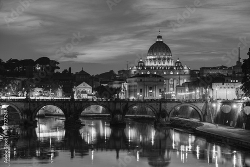 A black and white evening view of St. Peter's Basilica, Vatican City, Holy See, from a bridge over the Tiber river, Rome, Italy 
