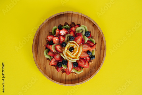 Organic healthy vegetarian berries cheesecake, red berries, kiwi, raspberry, strawberry, orange slices. Wooden plate on yellow background. Copy space