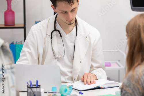 A doctor checks a book calendar for the date of the next follow-up appointment for a young teenage girl. The doctor s office