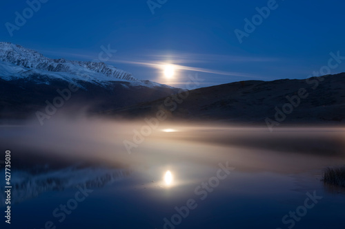 Picturesque misty moonlit night on Lake Dzhangyskol and reflection in the water. Russia, Altai Republic,