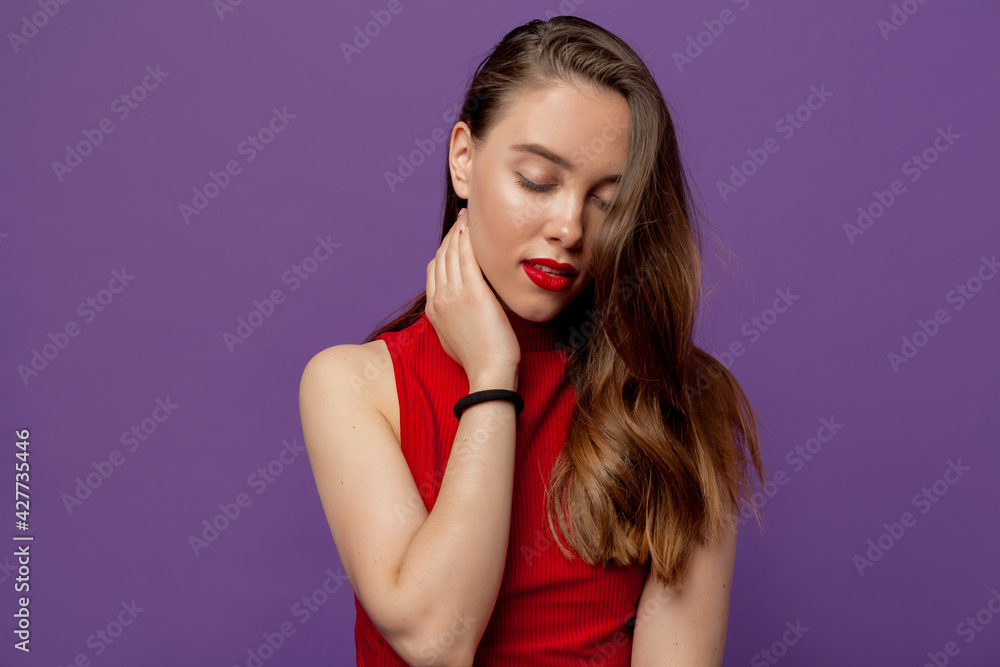 Sensitive pretty girl with wavy brown hair touching neck with closed eyes over violet backdrop