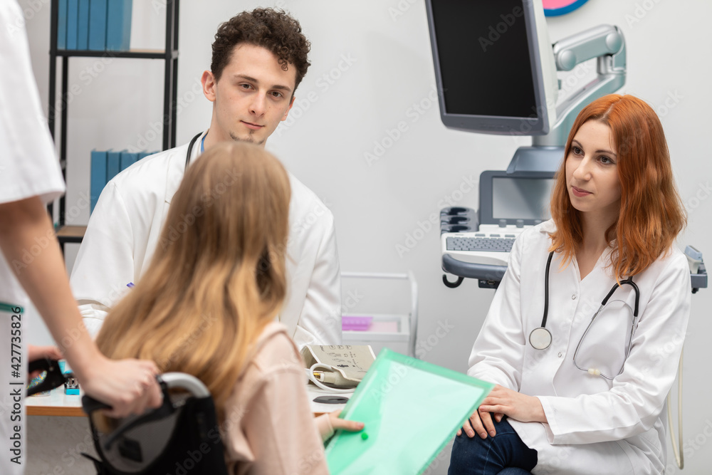 Fototapeta premium A nurse brought the teen in a wheelchair to the doctor's room. GP. The redheaded intern