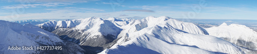 Breathtaking panoramic shot of mountain peaks covered in snow during the winter season. A blue sky with few white clouds can be seen in the background. Zakopane - Kasprowy Wierch © CameraCraft