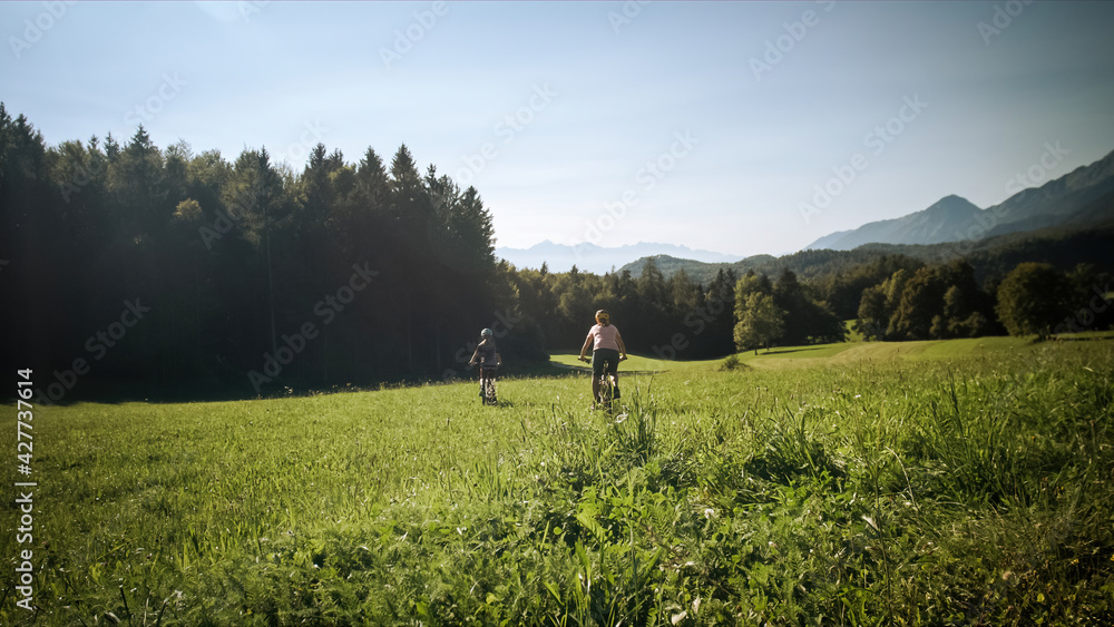 Fototapeta premium Two females on mountain bikes talking and looking at beautiful green nature.