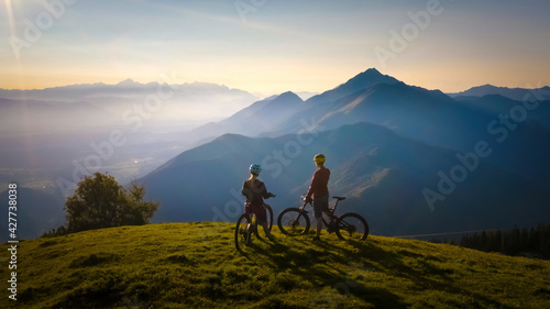 Two females on mountain bikes talking and looking at beautiful sunset photo