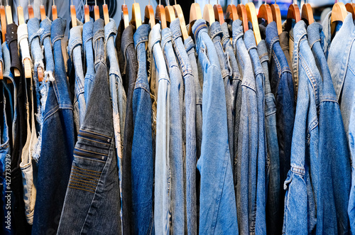 A lot of jeans jackets hanging on a hanger in the store. A row of jeans jackets in the store. Sale of jeans in the store on the counter. Texture of jeans