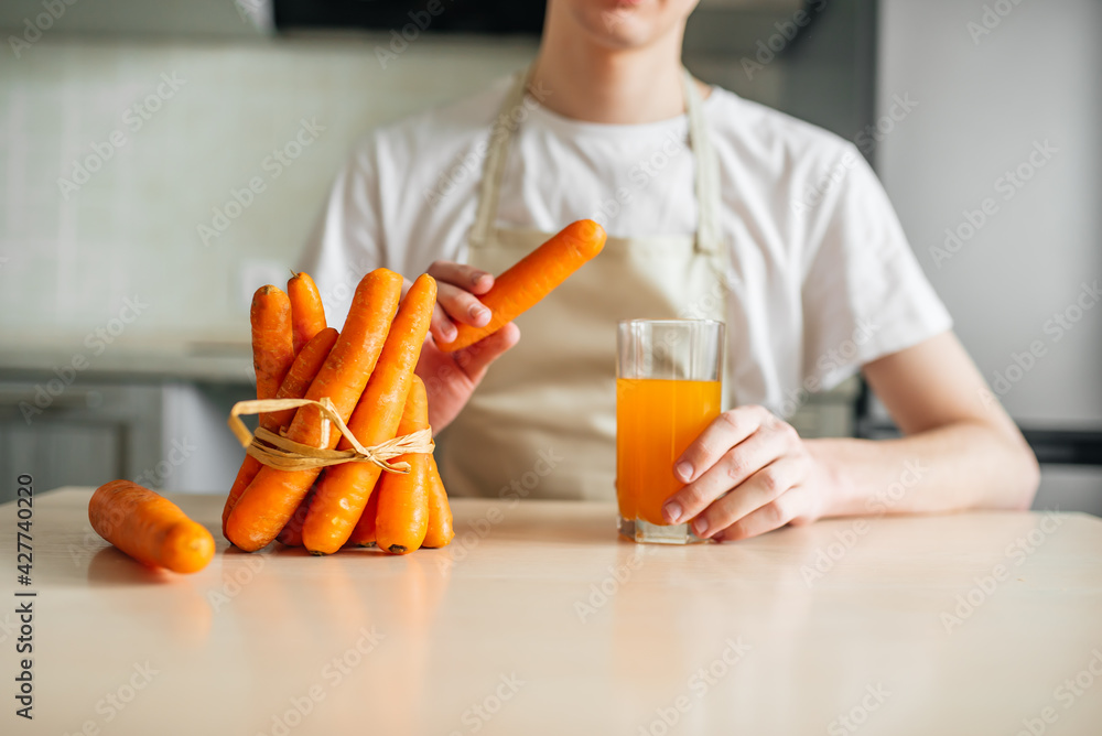 carrots and carrot juice in a glass beaker in the kitchen. Young guy and healthy food carrots and carrot juice in a glass beaker in the kitchen. Young guy and healthy food