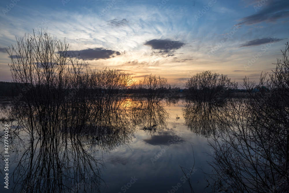 Evening landscape with a river and bushes. The sunset is reflected in the river. Evening landscape with a river and bushes. The sunset is reflected in the river.