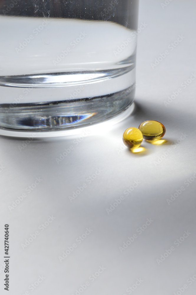 a glass beaker and two yellow tablets with vitamins. close-up. a glass beaker and two yellow tablets with vitamins. close-up.
