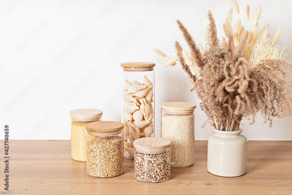 Assortment of grains, cereals and pasta in glass jars and dry herbs on wooden table. Healthy balanced food ingredients, sustainable lifestyle, zero waste storage idea, eco friendly concept.