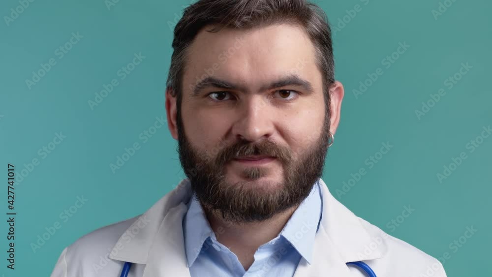 Satisfied doctor man in medical coat nods head approvingly. Positive smiling doc, body language concept. Blue studio background. Satisfied doctor man in medical coat nods head approvingly. Positive smiling doc, body language concept. Blue studio background.