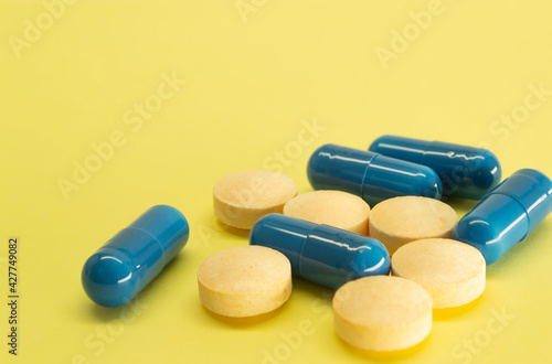 Orange pills and blue capsules on a yellow background with space for text. Medicine image. Healthcare.
