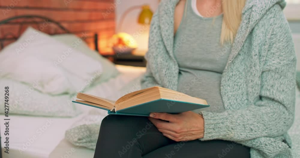 Close up hands young pregnant woman having rest on the bed among pillows reading book in the cozy room at home. Indoor Close up hands young pregnant woman having rest on the bed among pillows reading book in the cozy room at home. Indoor