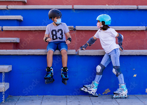 Two pre-teens, a boy and a girl, rest after skating on some bleachers, while they talk to each other.
