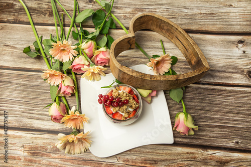 Close-up of a healthy yogurt with muesli and fruits in a lovely arrangement with flowers on a wooden background