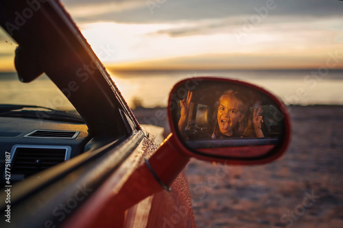 Autumn road trip, freedom and family traveler. Pretty girl sitting in the car on the bank of sea, rest and leisure, looking at beautiful sunset after rain, drops on windshield, fall outdoor lifestyle