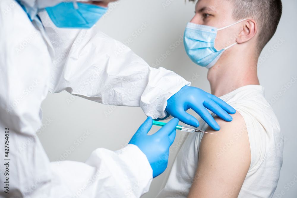 A doctor dressed in a protective suit vaccinates a patient against coronavirus. A doctor dressed in a protective suit vaccinates a patient against coronavirus.