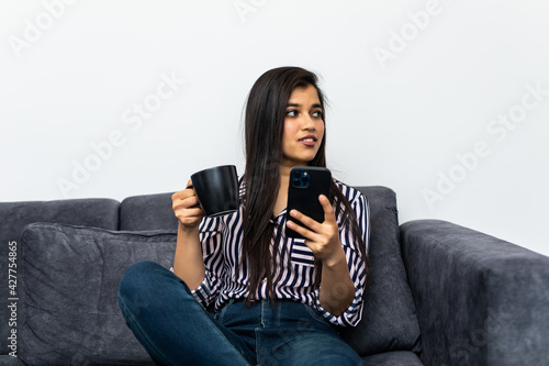 Portrait beautiful young asian woman use mobile smartphone or cellphone with coffee cup on sofa living room interior