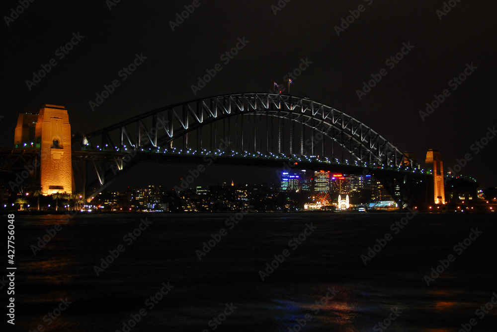 View of the Sydney Harbour Bridge illuminated at night with the city skyline in the background. 