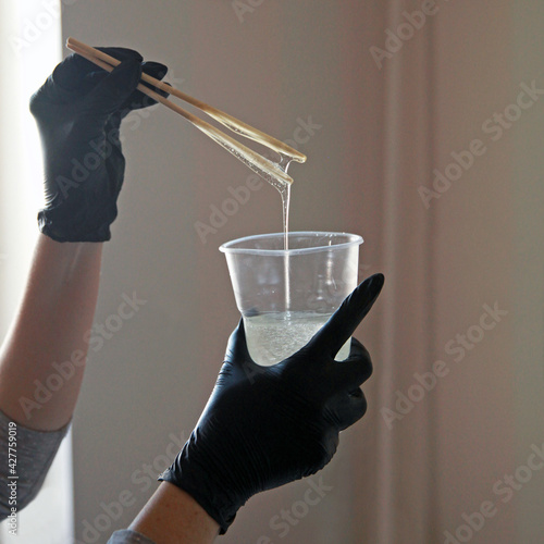 Epoxy resin, a girl in gloves painstakingly mixes the liquid in a plastic cup, against the window.