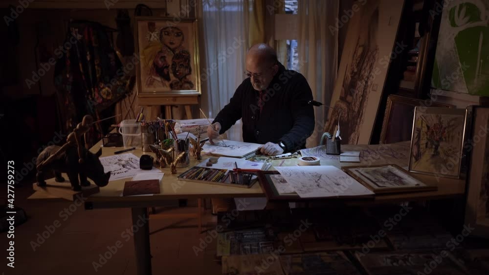 Cinematic style with smooth camera movement approaching of an artist working in studio. Middle-aged man making creative artwork, painting in watercolor with brush. Cinematic style with smooth camera movement approaching of an artist working in studio. Middle-aged man making creative artwork, painting in watercolor with brush.