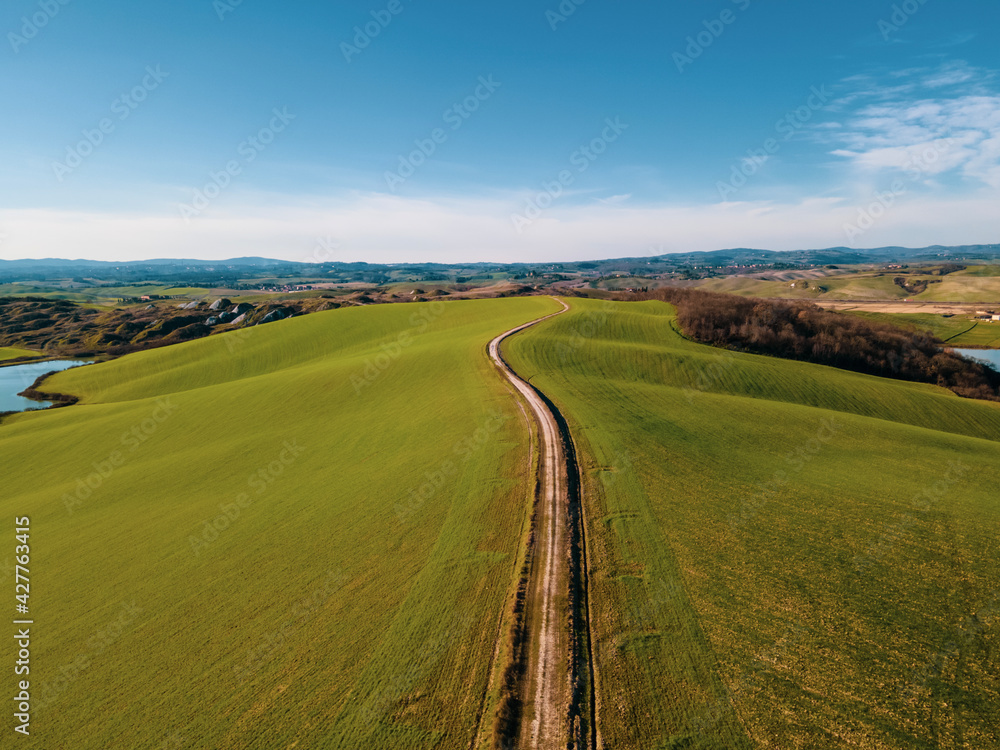 Aerial view of a calm landscape with green hills, dirt road and a lake. Drone shot  