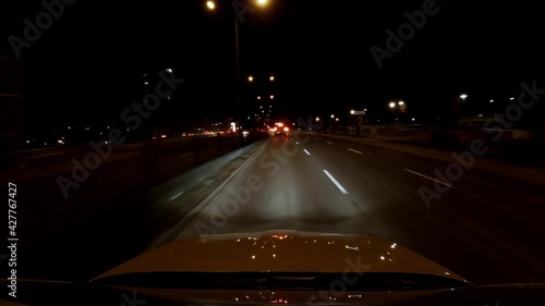 View from a car driving through a road at night. Red backlights in the distance, passing by a gas station photo