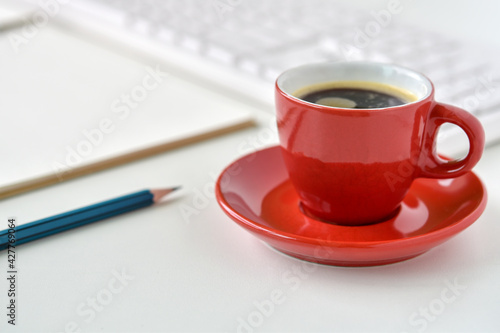 Black coffee in red cup on table desk with pencil, sketchbook and keyboard is elements.