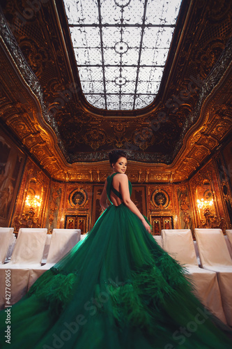 Portrait of a beautiful young girl in a Haute couture green dress standing in a luxurious gold and bronze interior.