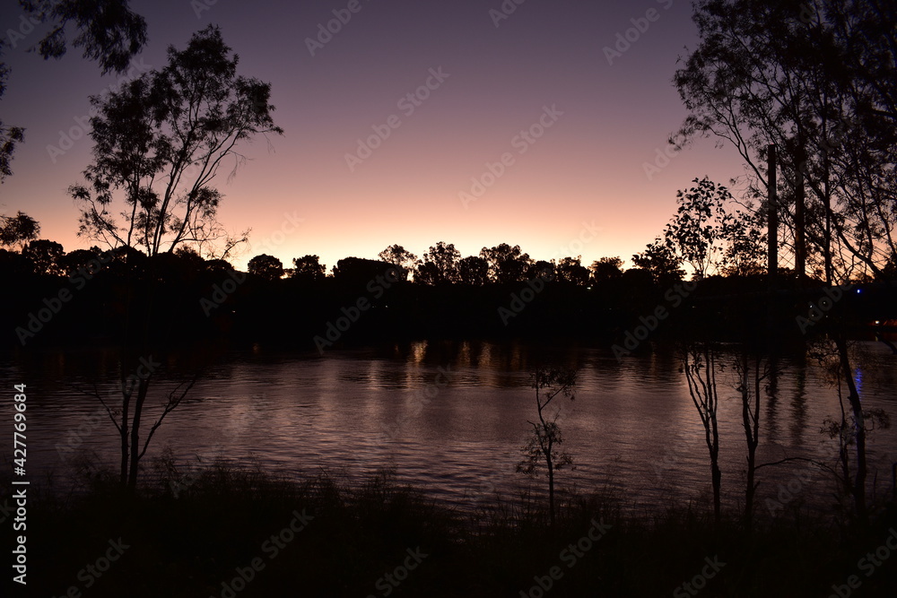 Wide slow-flowing river at dusk with tree silhouettes