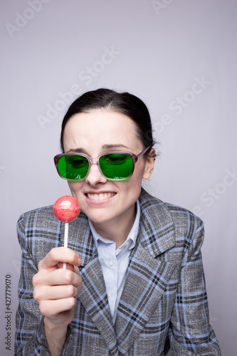 woman maneger in suit in a cage and green glasses eating a lollipop © Диана Шиловская