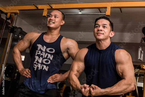 Two friends enjoy a friendly posedown after training, doing standing relaxed and most muscular poses. Having fun and camaraderie at the gym. photo