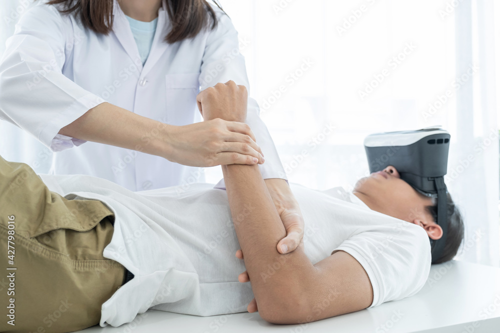 Obraz premium Female doctor hands doing physical therapy By extending the arm of a male patient with VR box, the concept of technology helped the feeling as if a doctor came to treat him at home