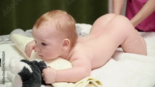 The masseuse gives a leg massage to a happy child (boy). The baby lies on his belly, holds a soft toy in his hands. Baby ticklish
