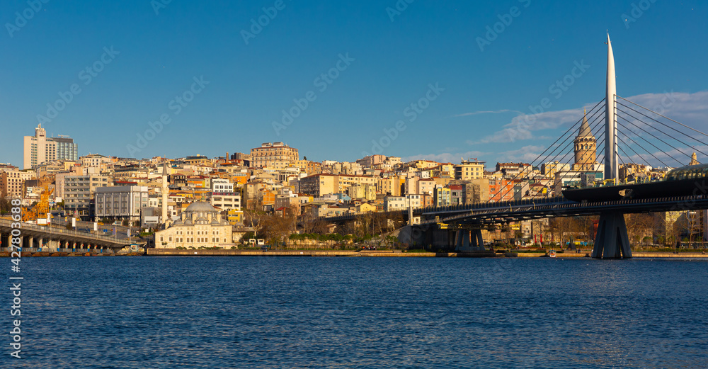 Fototapeta premium Scenic view of modern cityscape of Beyoglu district in Istanbul across Bosphorus and Golden Horn bay with views of cable-stayed metro bridge on sunny winter day, Turkey