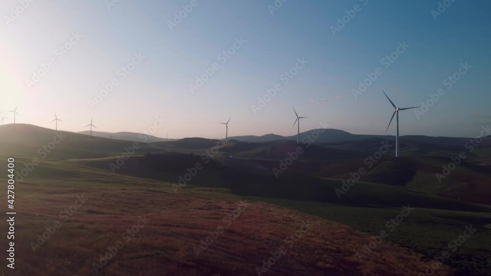 Drone flying backwards on the countryside, with wind turbines on the background Drone flying backwards on the countryside, with wind turbines on the background