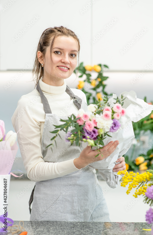 Smiling florist wearing apron arranging a bouquet of beautiful colorful flowers inside her floral shop Smiling florist wearing apron arranging a bouquet of beautiful colorful flowers inside her floral shop