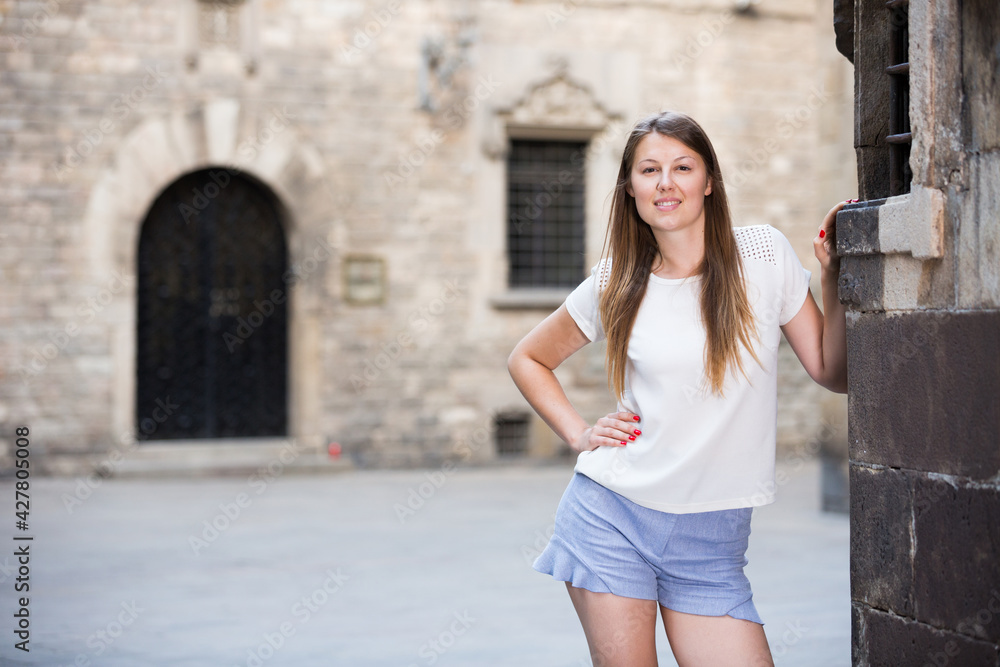 Romantic attractive girl walking on old town streets leaning against stone wall