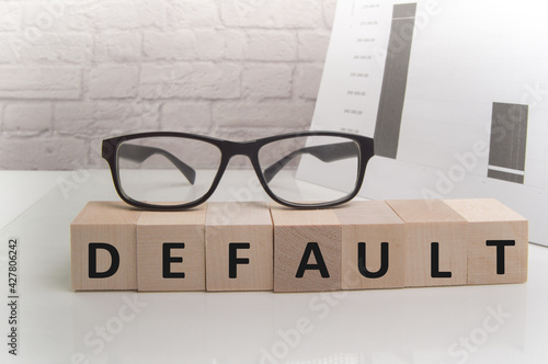 The word default is written on wooden cubes standing on the white surface of the table, THE GLASSES are on the cubes