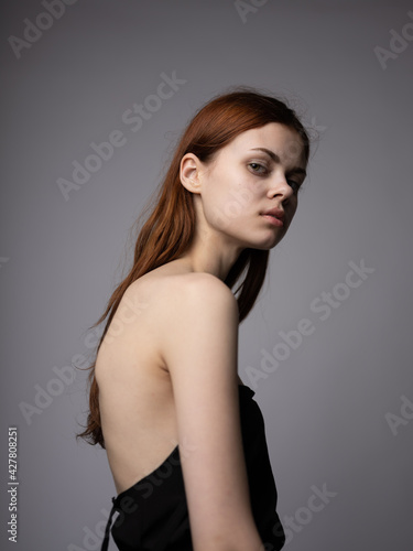 Portrait of a beautiful red-haired woman with bare shoulders on a gray background close-up