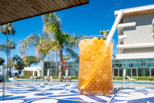 Fresh alcoholic cocktail with ice in glass on swimming pool. Hard strong drink on sunlight with palms. Concept summer luxury holiday and travel.