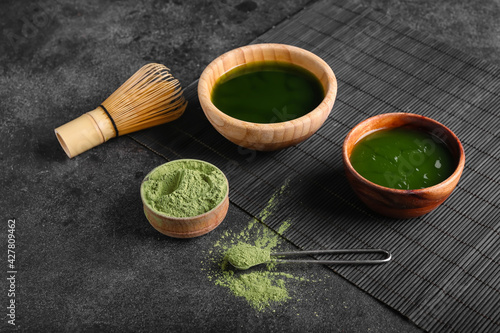 Bowls with matcha tea, powder and chasen on dark background
