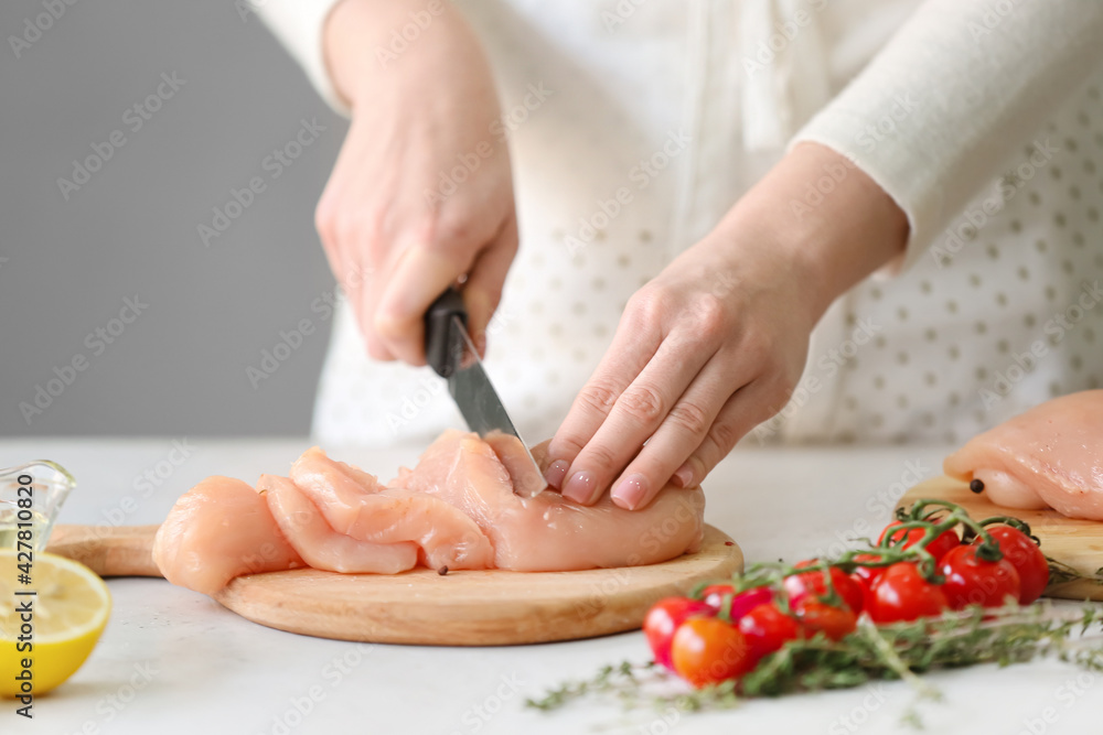 Woman cutting raw chicken fillet on table