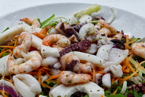 Fresh salad from seafood: octopus, cuttlefish, shrimp. Sea salad on white dish. Close-up