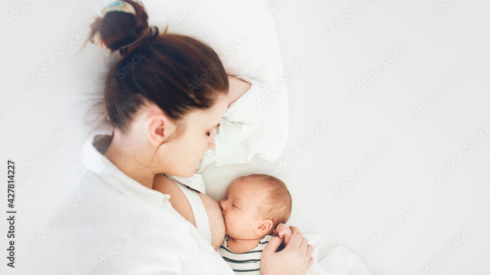 mom and newborn baby, mother breastfeeds the baby lying on a white background on the bed in the bedroom, top view and banner mom and newborn baby, mother breastfeeds the baby lying on a white background on the bed in the bedroom, top view and banner
