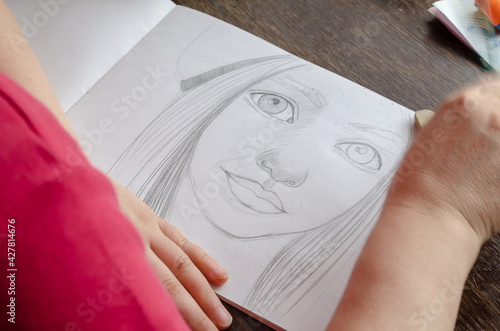 An adult woman draws a portrait with a pencil on paper.