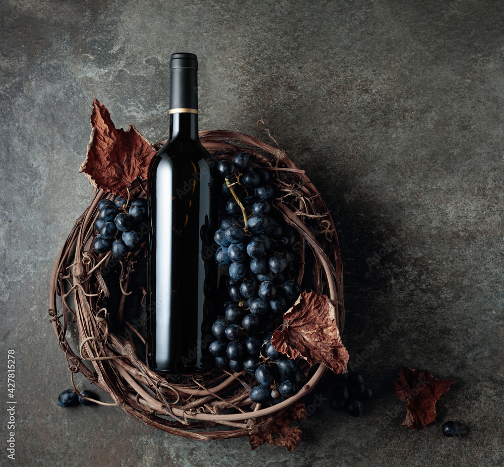 Bottle of red wine with grapes and dried vine leaves on an old stone background. - obrazy, fototapety, plakaty 